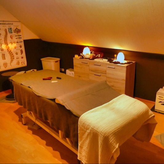 Behandlungsraum von Mediwellness in Neuenkirchen mit Massageliege, warmem Licht und Wirbelsäulen-Lehrtafel